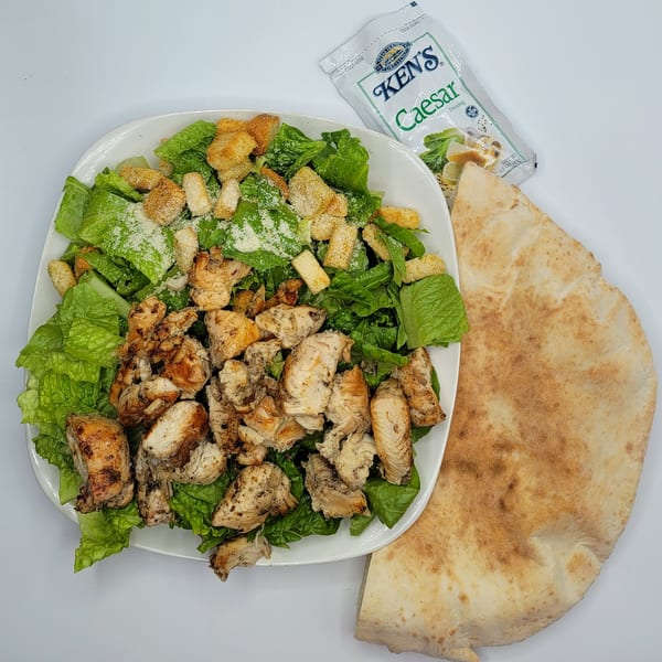 Chicken Caesar salad with croutons, parmesan, a side of pita bread, and Ken's Caesar dressing.