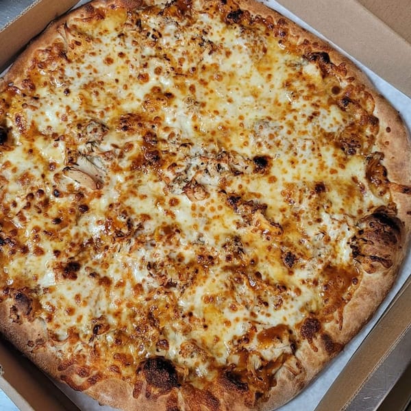 A whole Timo's Pizza with melted cheese and chicken, in a cardboard delivery box.