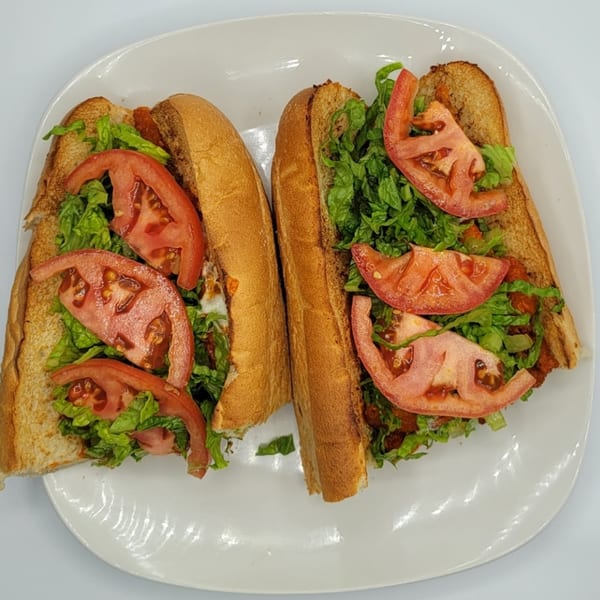 Two toasted subs filled with lettuce, sliced tomatoes, and meat on a white plate.